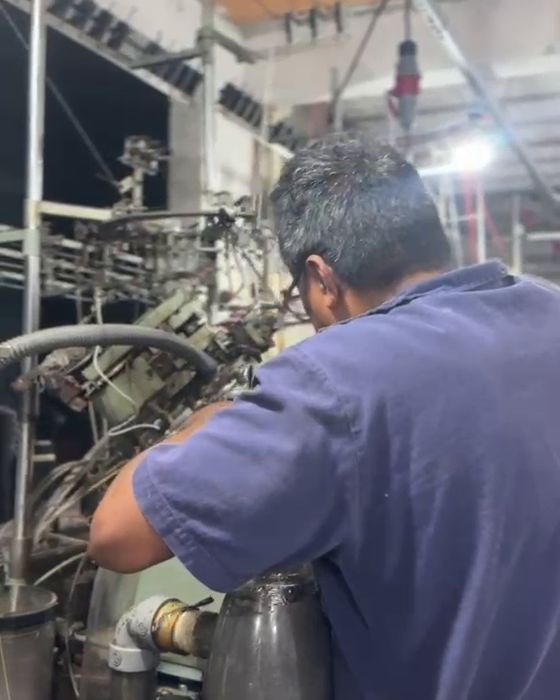 Operador ajustando máquina de meias na fábrica